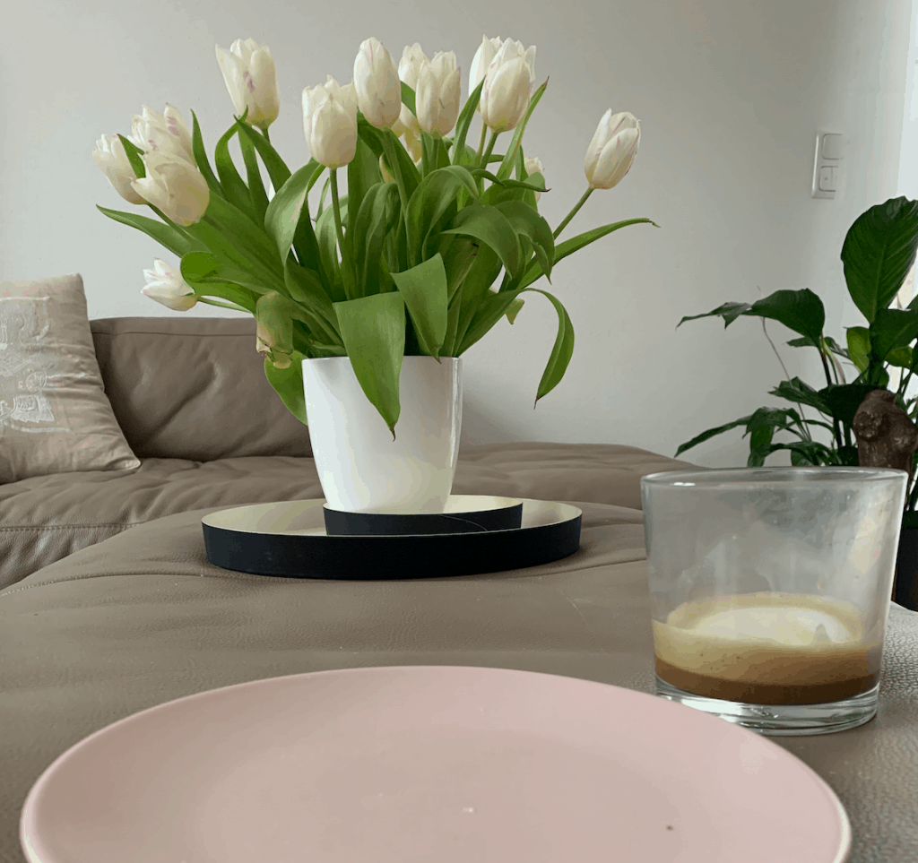 ein leerer rosafarbener Frühstücksteller daneben ein fast leeres Glas Kaffee dahinter ein Strauss weisser Tulpen